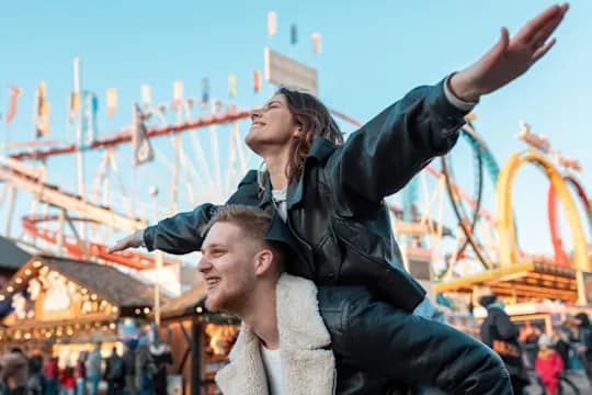 A cheerful-looking woman sits on a man's shoulders and spreads her arms